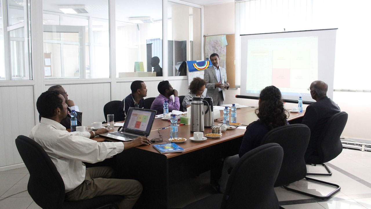 Male trainer looking at training participants who are looking at the screen at the front of the room