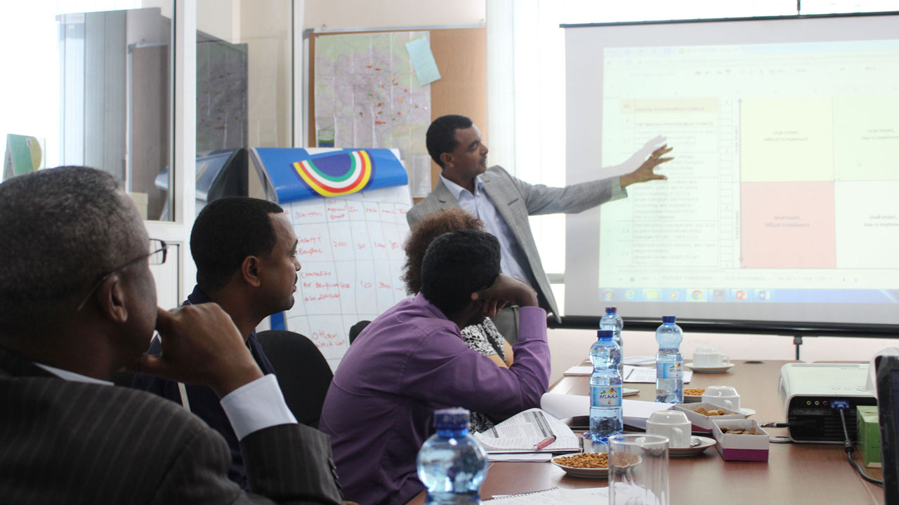 Male presenter leading training session, other participants seated and looking on at the screen