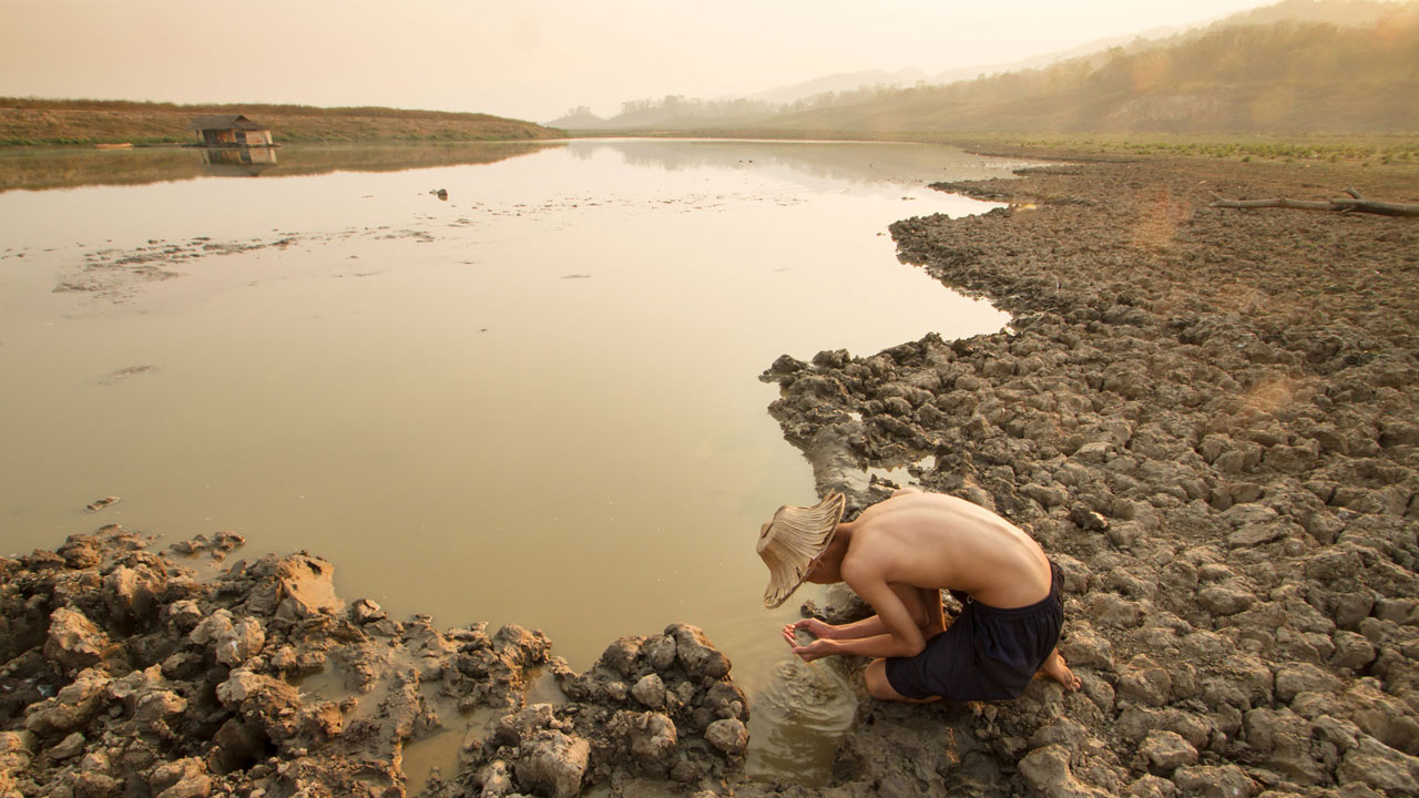 Man crouching down inspecting water from a drying lake