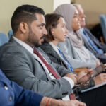 Businesspeople in suit making notes on tablet and paper while listening to speakers report at a conference