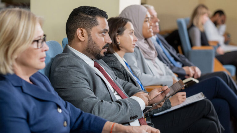 Businesspeople in suit making notes on tablet and paper while listening to speakers report at a conference