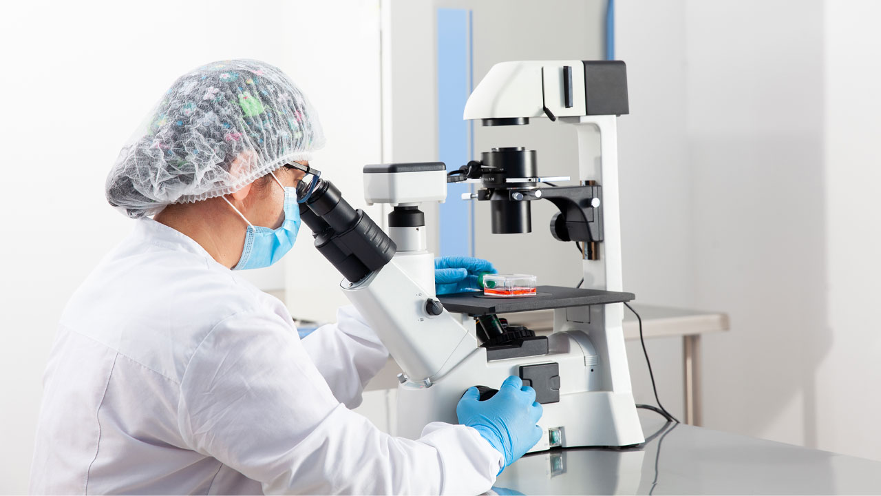 A person in a white lab coat is looking through a microscope