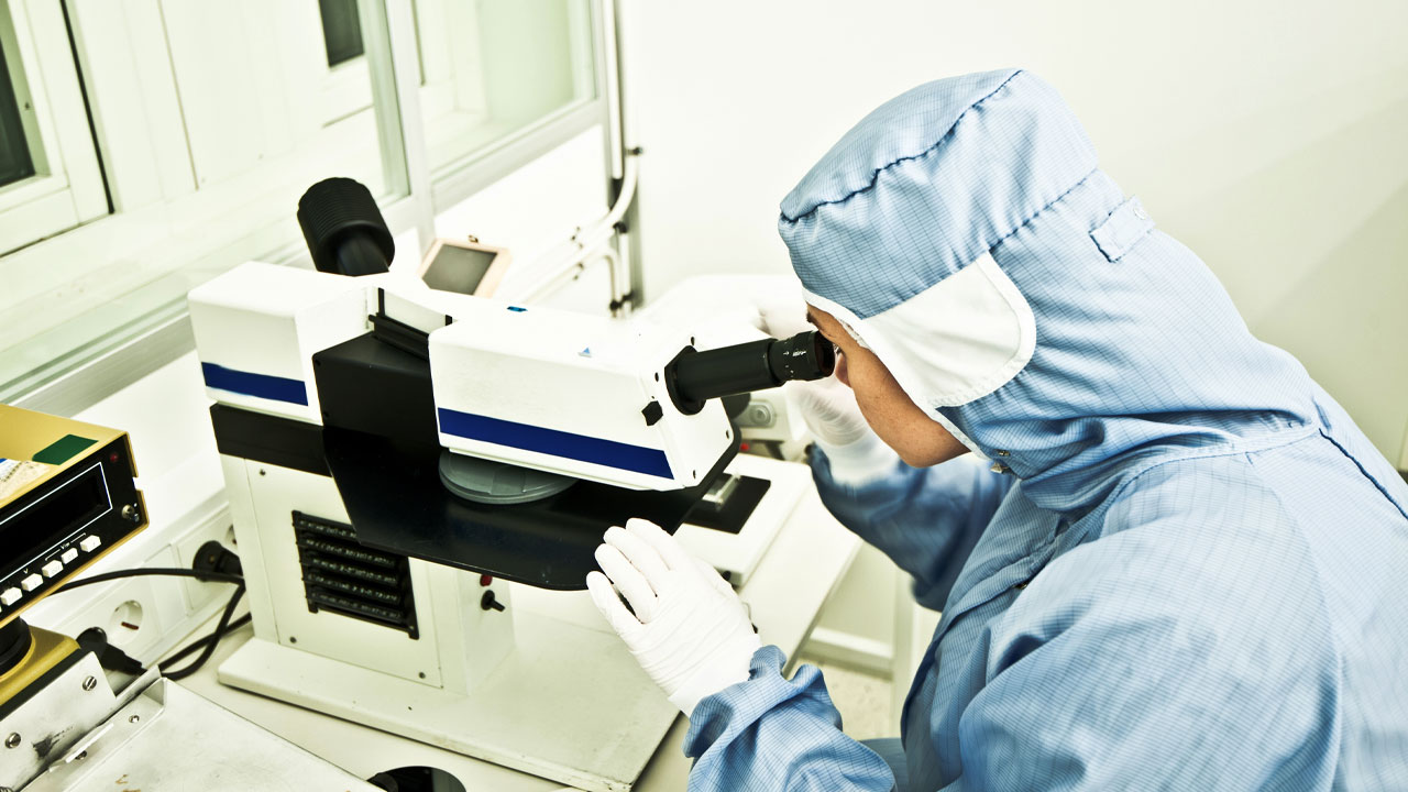 Scientist in a blue robe looking through the microscope