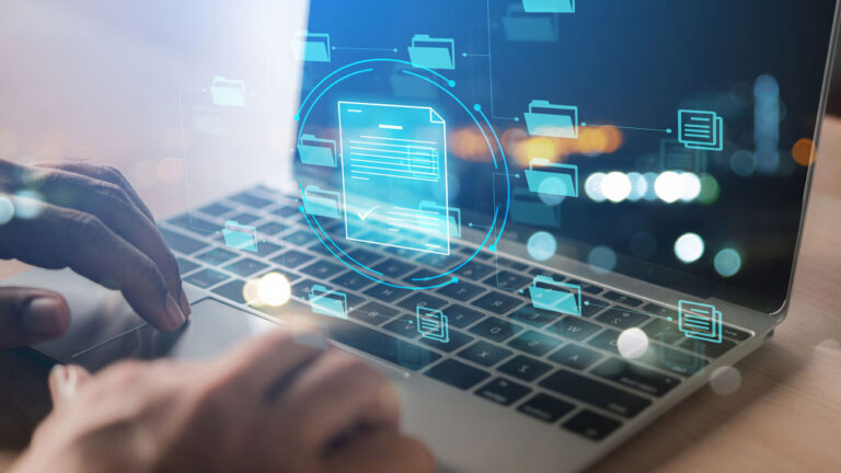 Hand pressing a key on a laptop and file and folders displayed in front of laptop screen