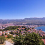 Macedonia flag flying above a town with sea to the right and mountains in the background