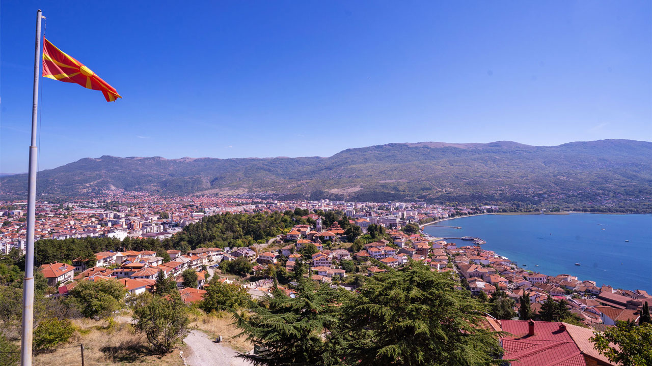 Macedonia flag flying above a town with sea to the right and mountains in the background