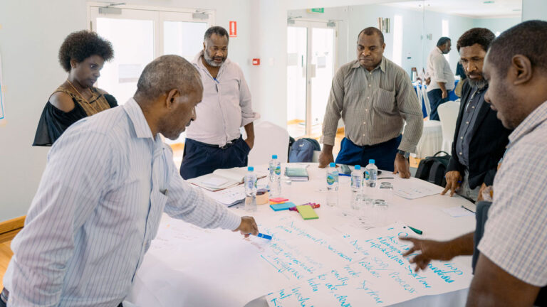 Group standing around a table and pointing at notes written on poster paper