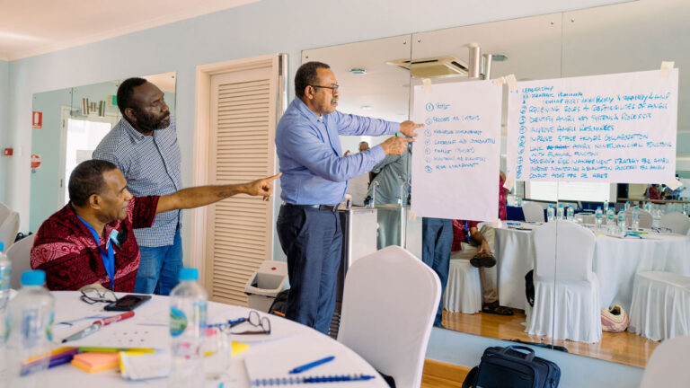 Three men looking and pointing at notes written on poster paper